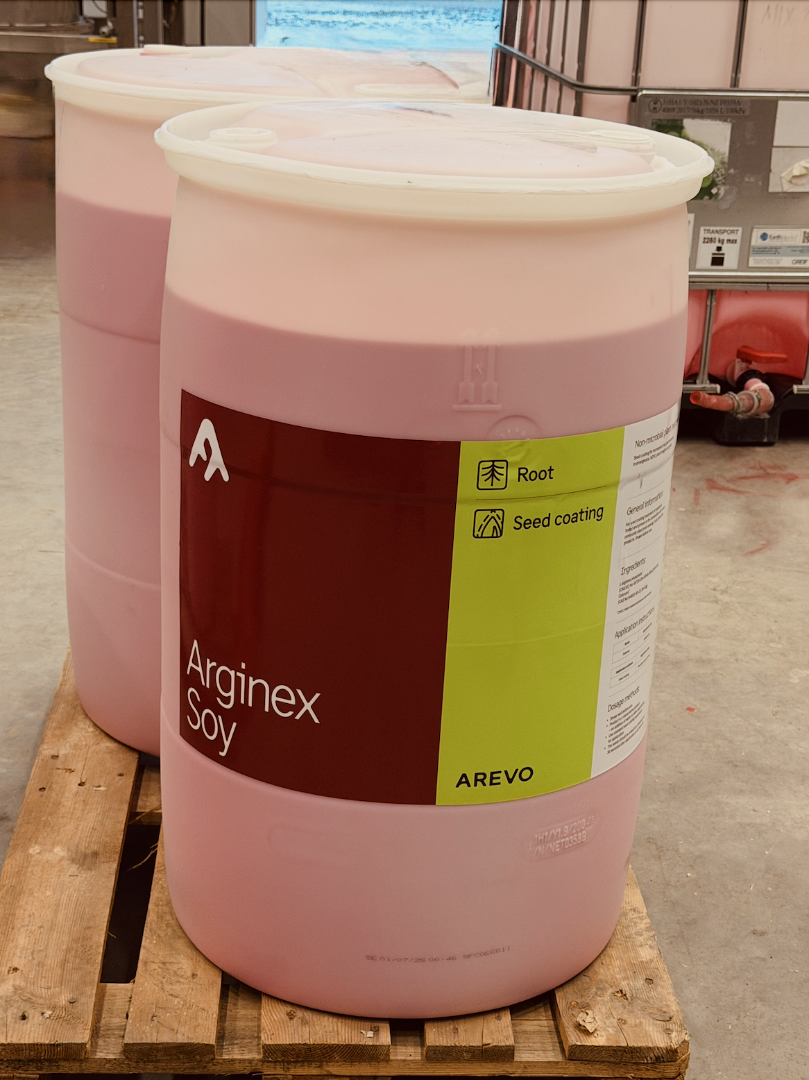 Two large pink plastic barrels labeled "Arginex Soy" with additional text indicating "Root" and "Seed coating" on a green and maroon label, placed on a wooden pallet in an industrial or warehouse setting.